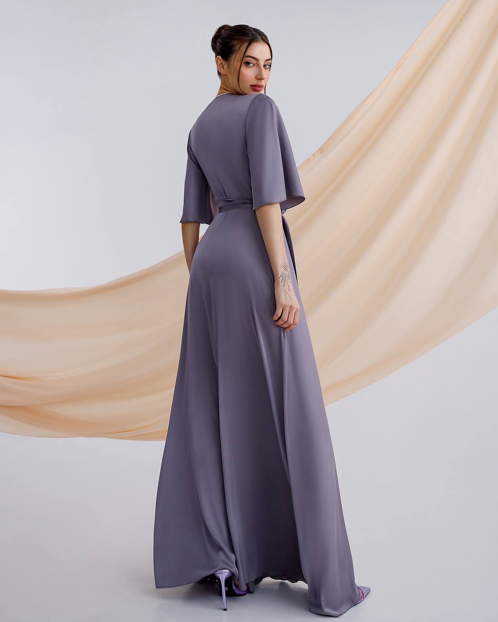 a woman in a long dress standing in front of a beige background
