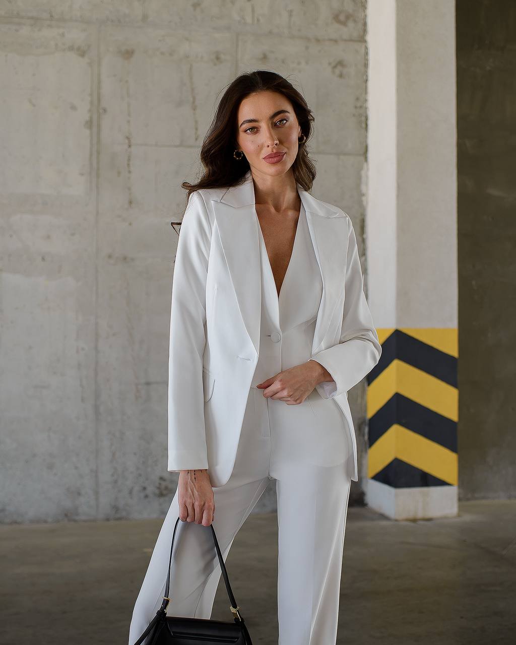 a woman in a white suit holding a black purse