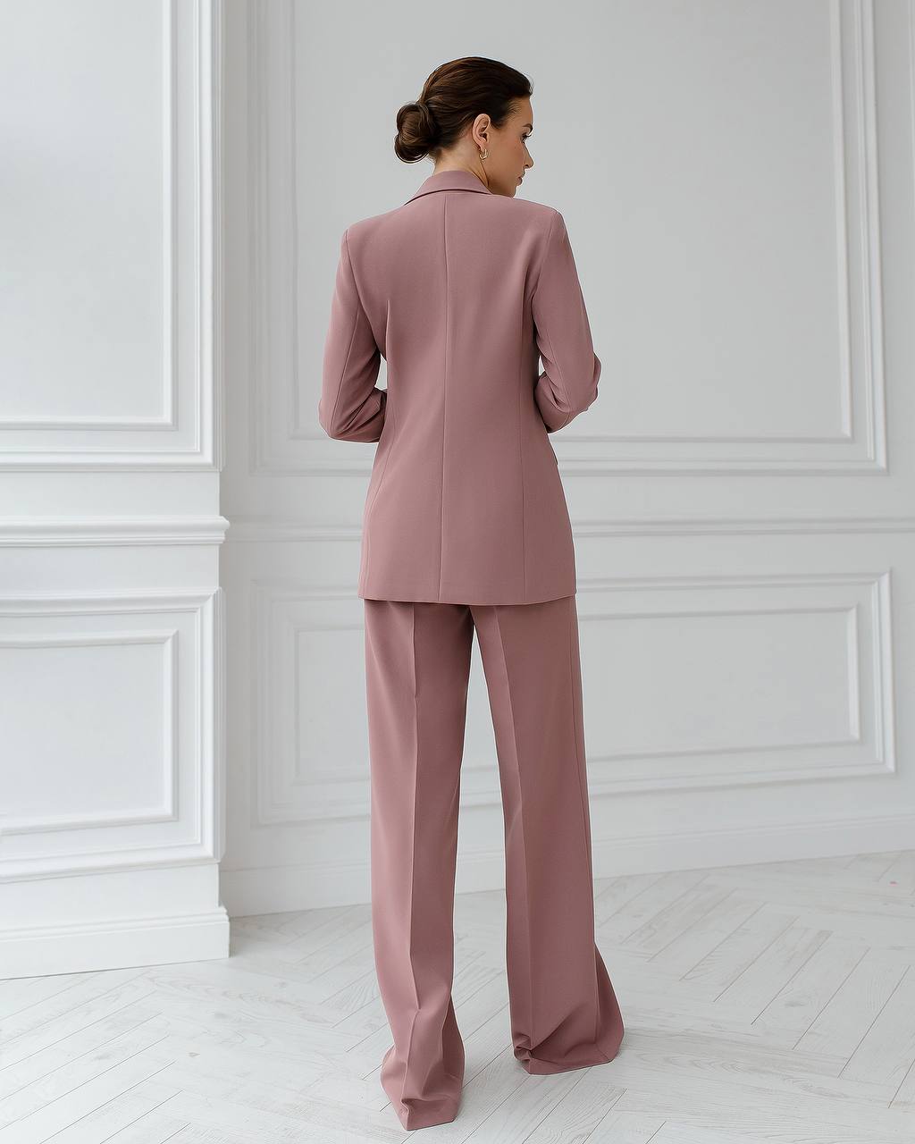 a woman in a pink suit stands in a white room