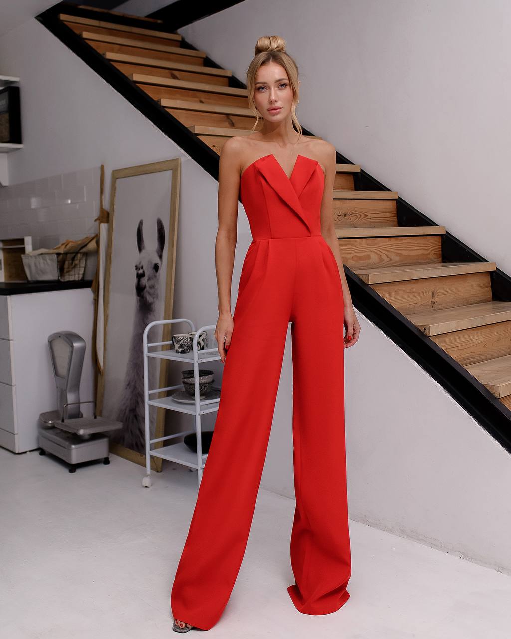 a woman in a red jumpsuit standing in front of a staircase