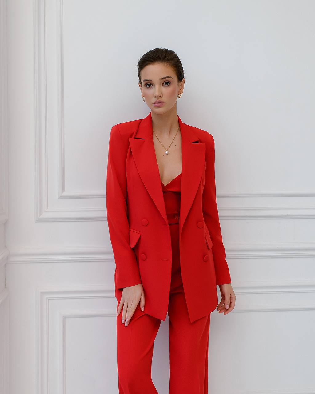 a woman in a red suit standing in front of a white wall