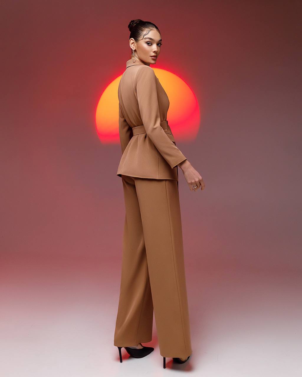 a woman in a tan suit standing in front of a red sun