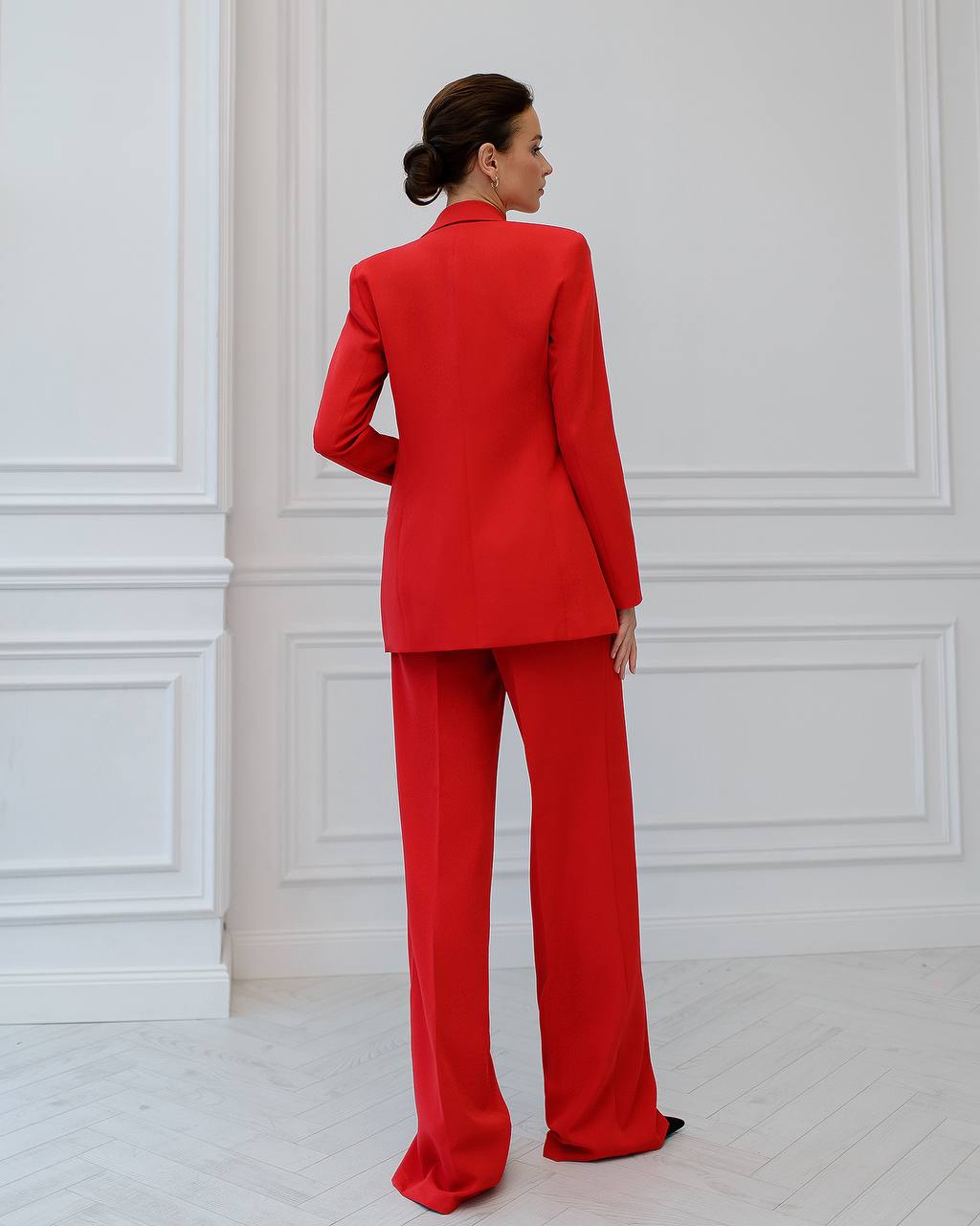 a woman in a red suit stands in a white room