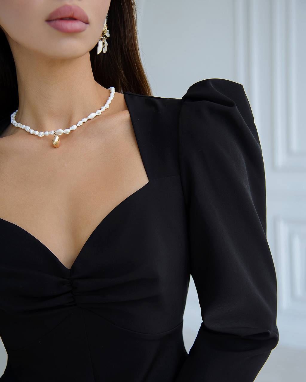 a woman in a black dress wearing a pearl necklace