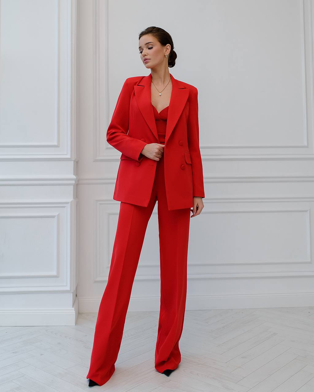 a woman in a red suit stands in front of a white wall
