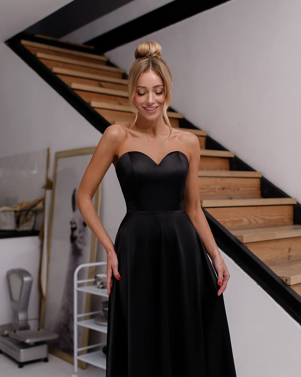 a woman in a black dress standing in front of a staircase