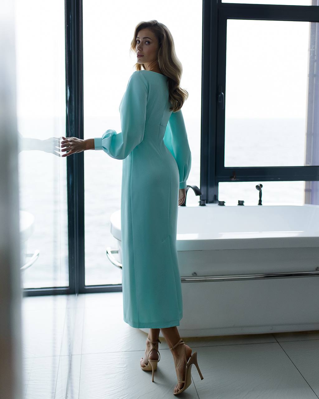 a woman in a blue dress standing in front of a window