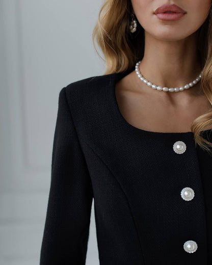 a woman wearing a pearl necklace and a black jacket
