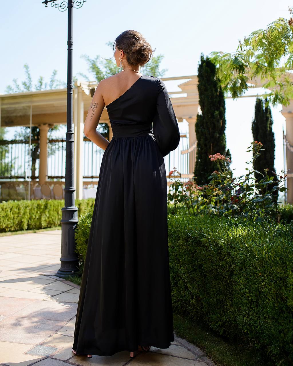 a woman in a long black dress standing on a sidewalk