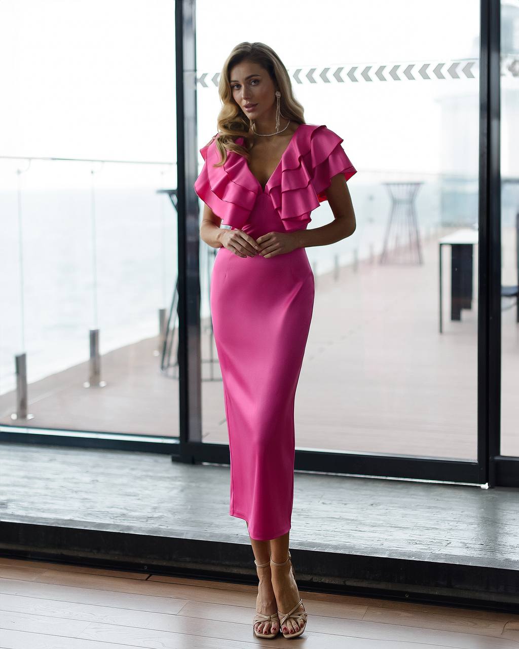 a woman standing in front of a window wearing a pink dress