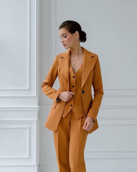 a woman in an orange suit stands in front of a white wall