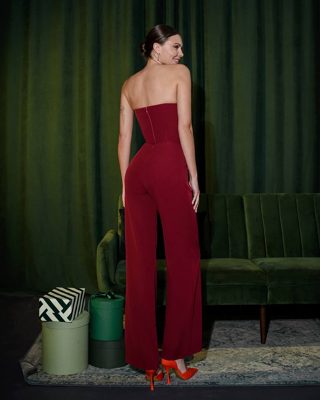 a woman in a red jumpsuit standing in front of a green couch