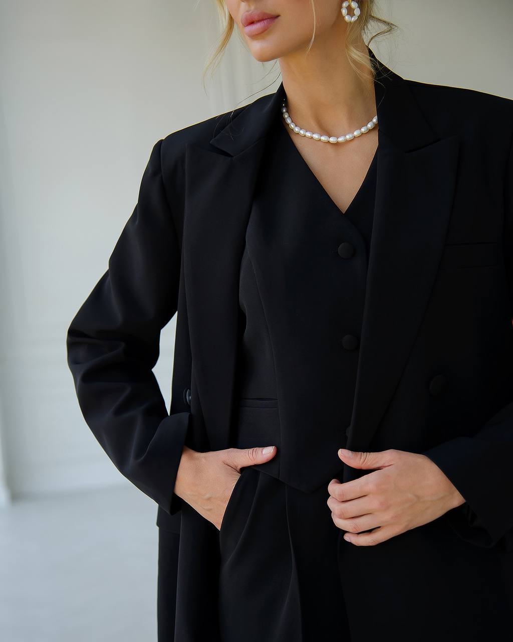 a woman wearing a black suit and pearl necklace