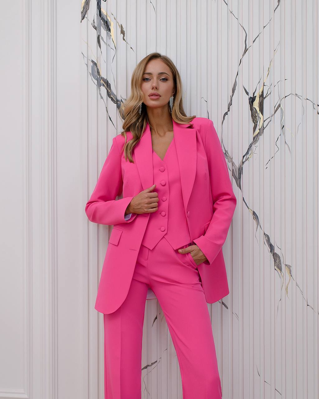 a woman in a pink suit leaning against a wall