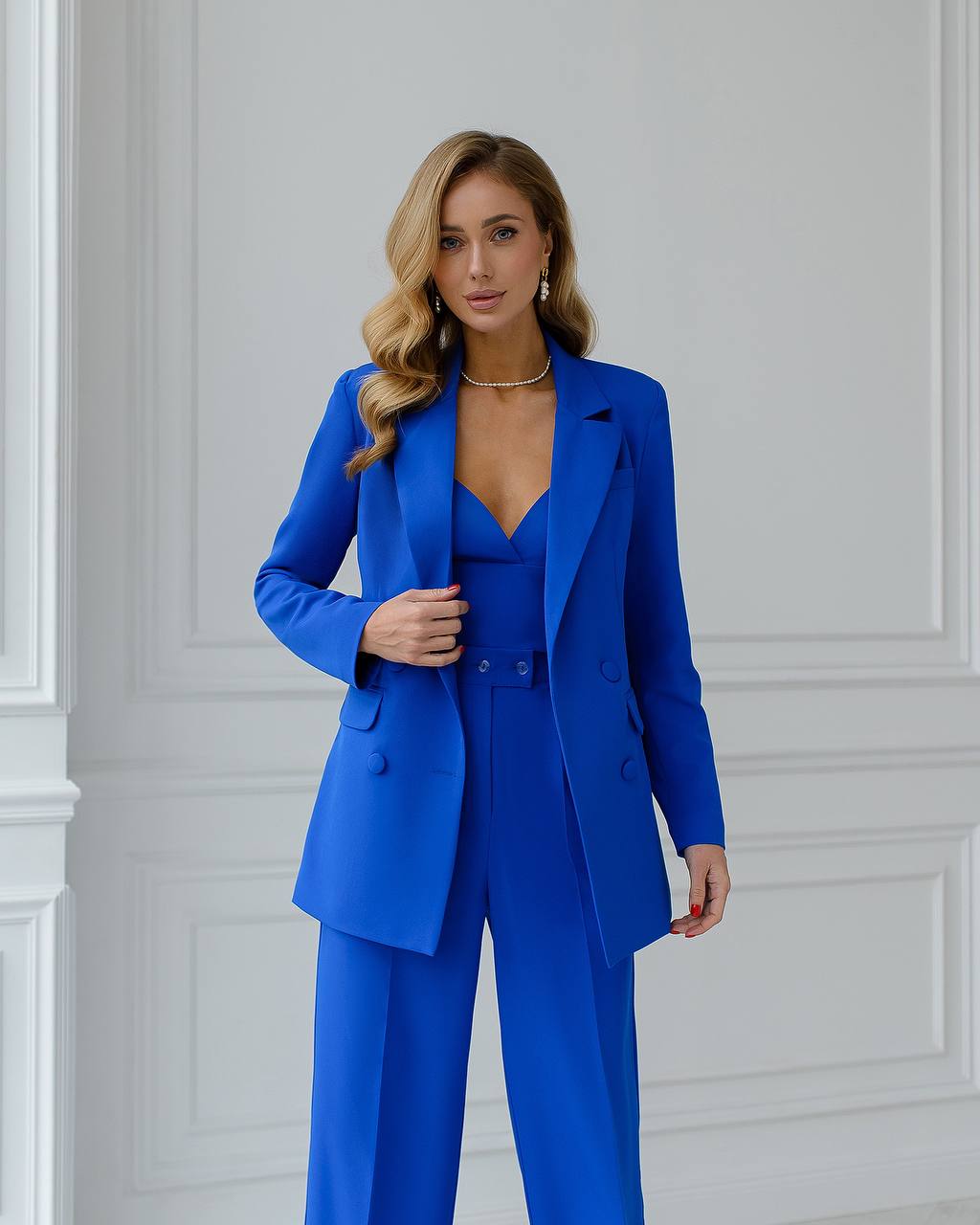 a woman in a bright blue suit stands in front of a white wall