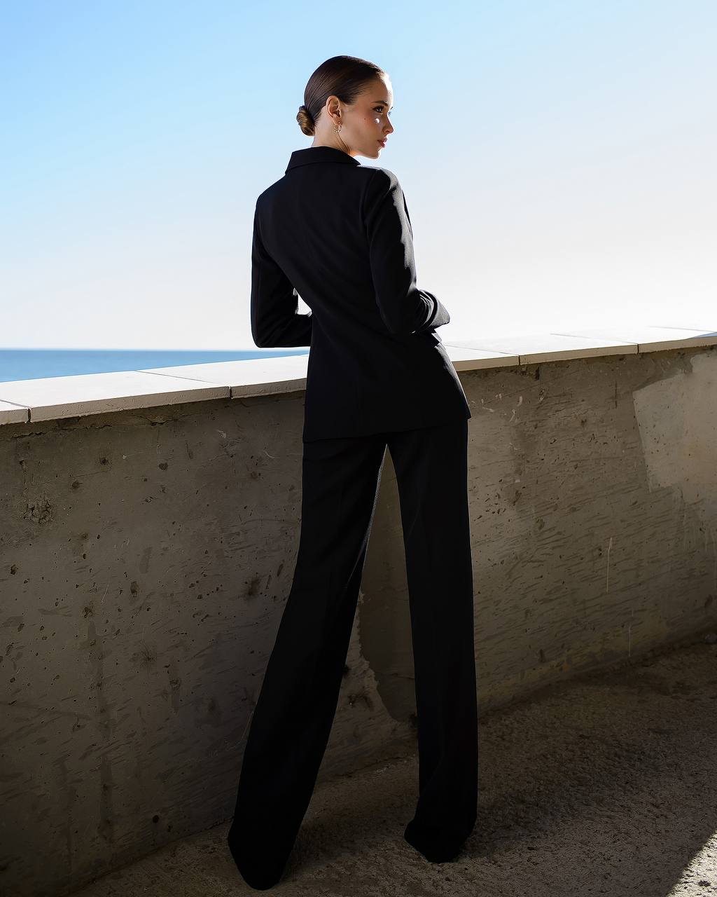 a woman in a black suit leaning against a wall