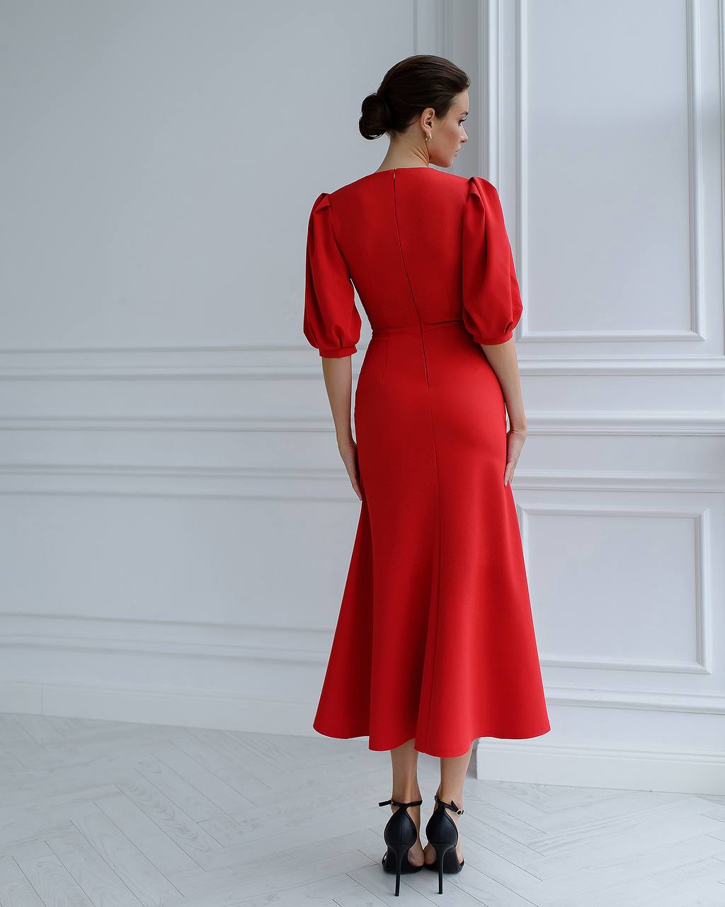 a woman in a red dress stands in front of a white wall