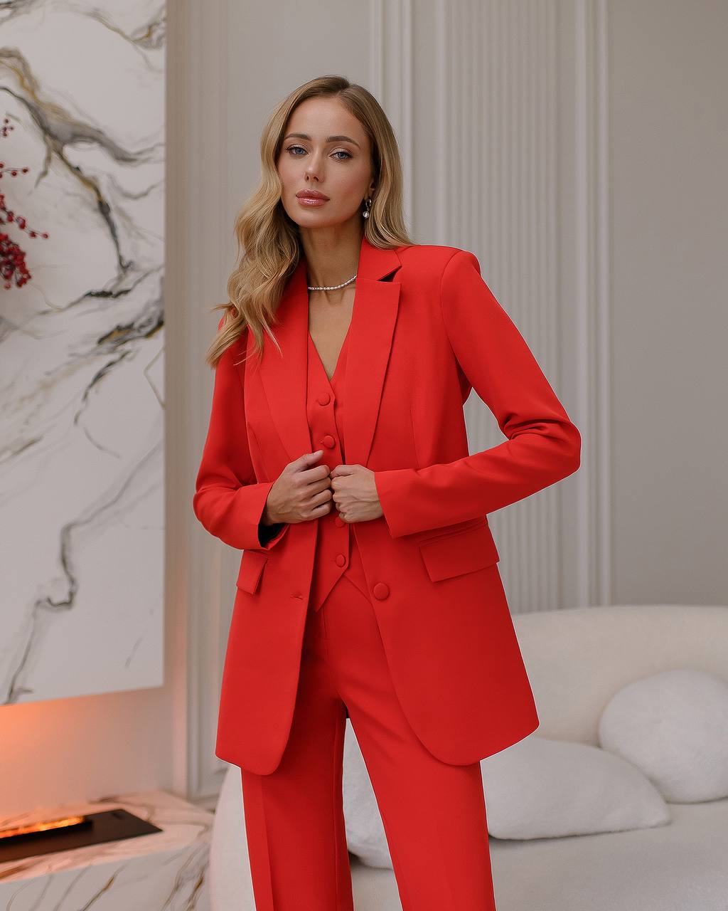 a woman in a red suit stands in front of a fireplace
