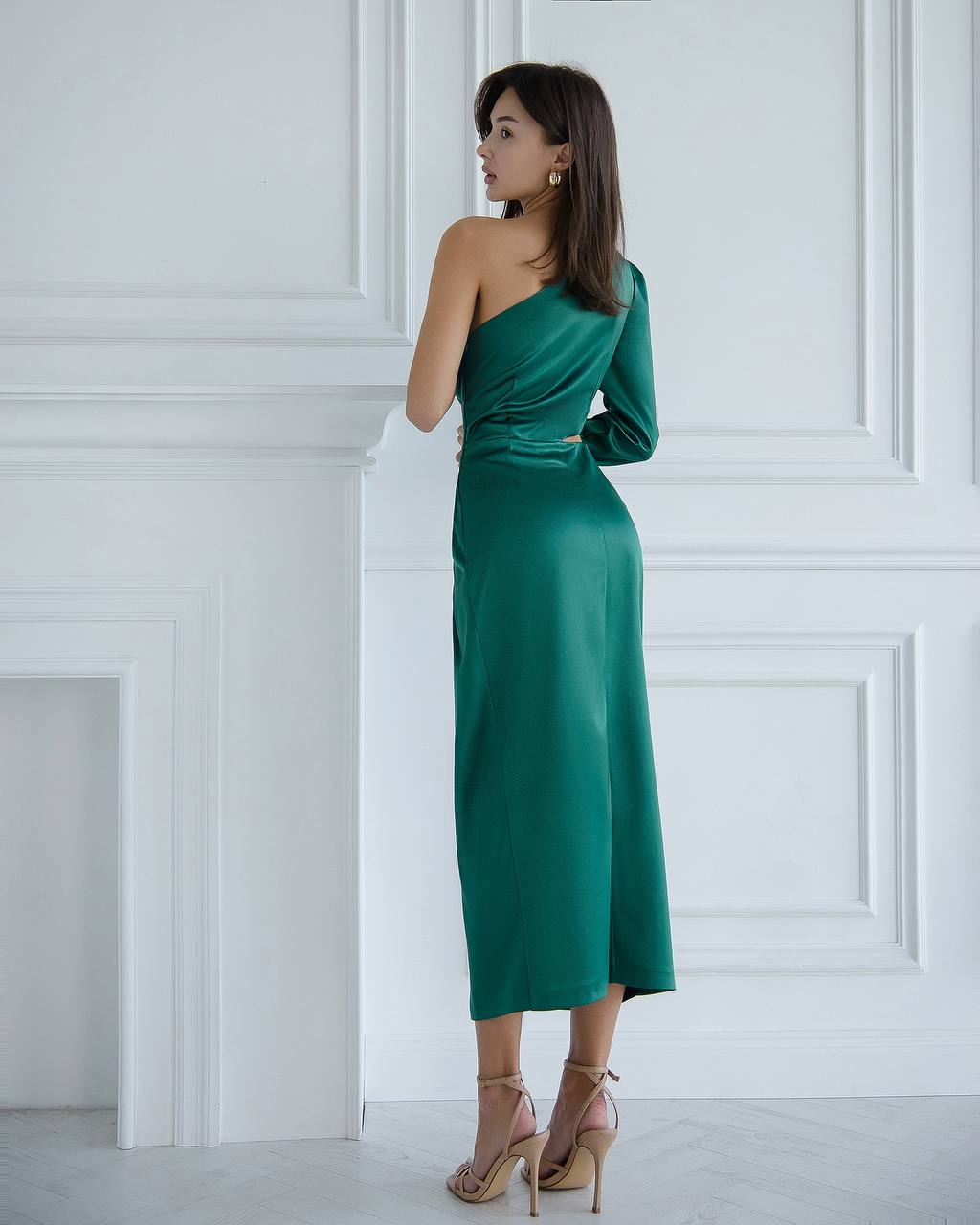 a woman in a green dress is leaning against a wall