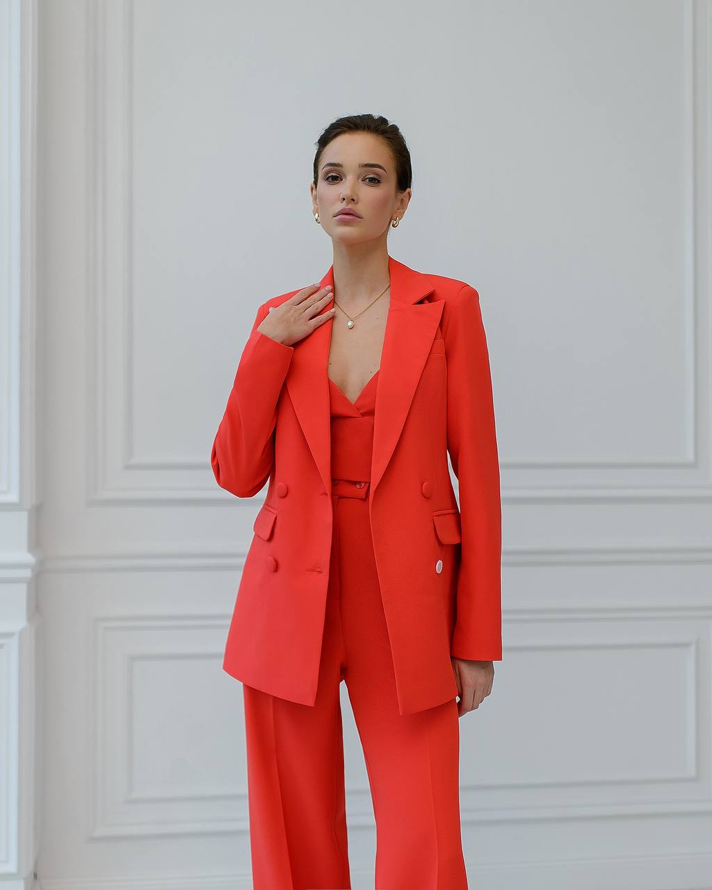 a woman in a red suit stands in front of a white wall