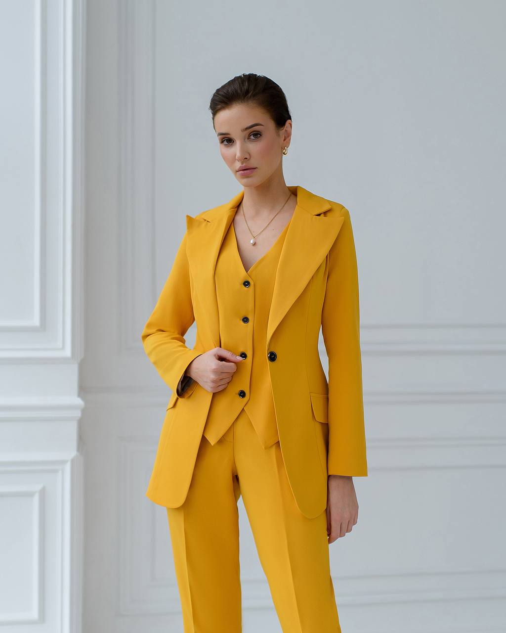 a woman in a yellow suit standing in front of a white wall