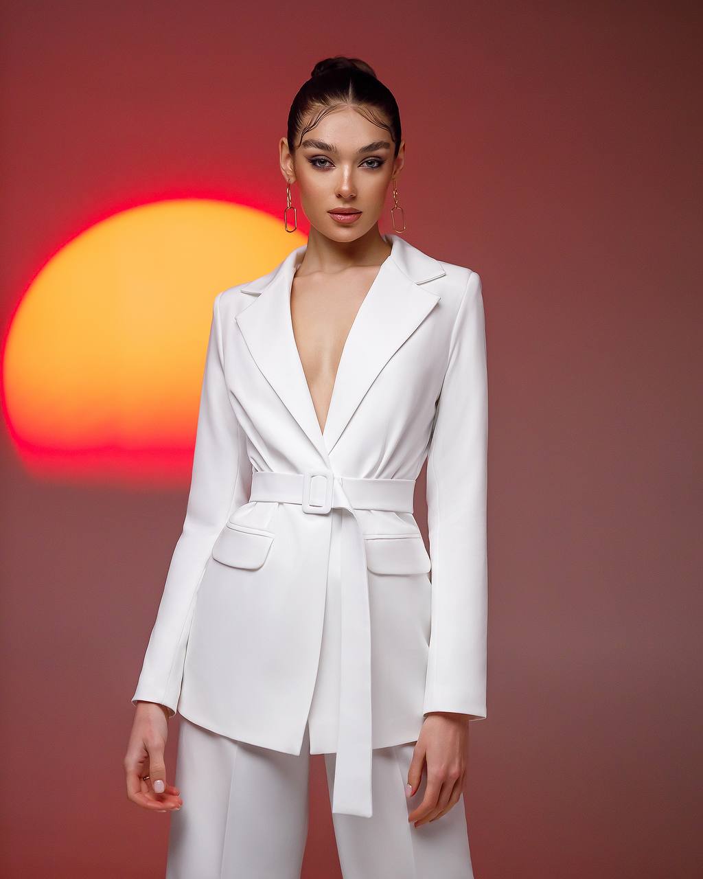 a woman in a white suit standing in front of a sunset