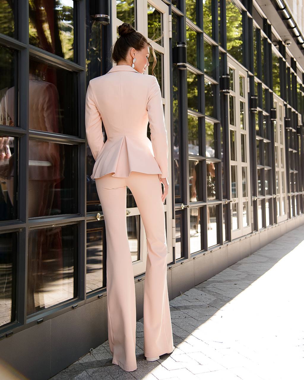 a woman in a pink suit leaning against a building