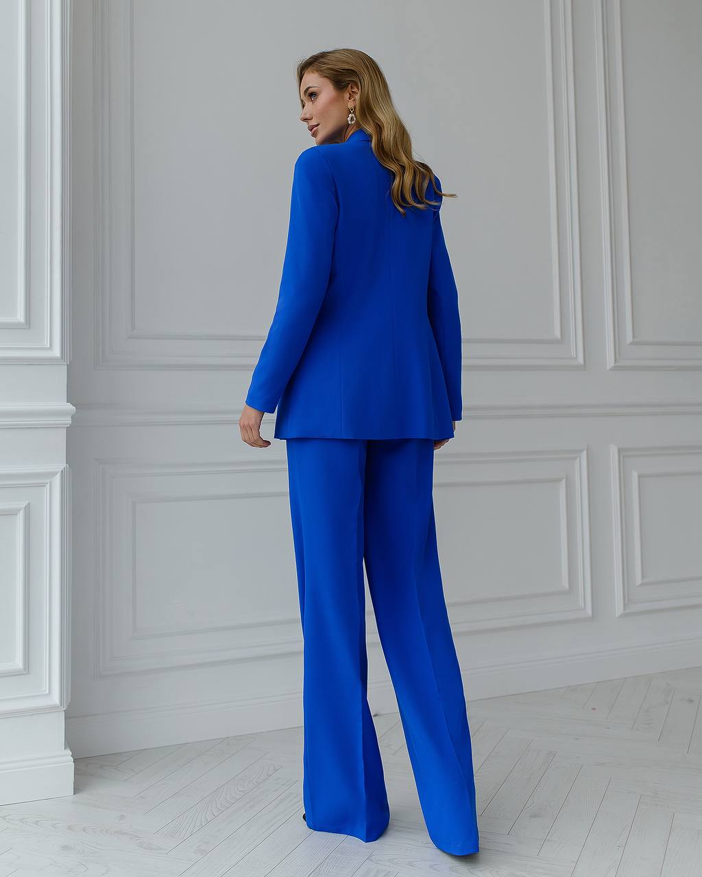 a woman in a blue suit stands in a white room