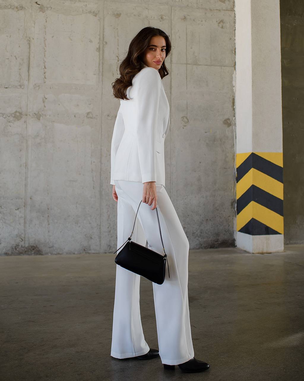 a woman in a white suit holding a black purse