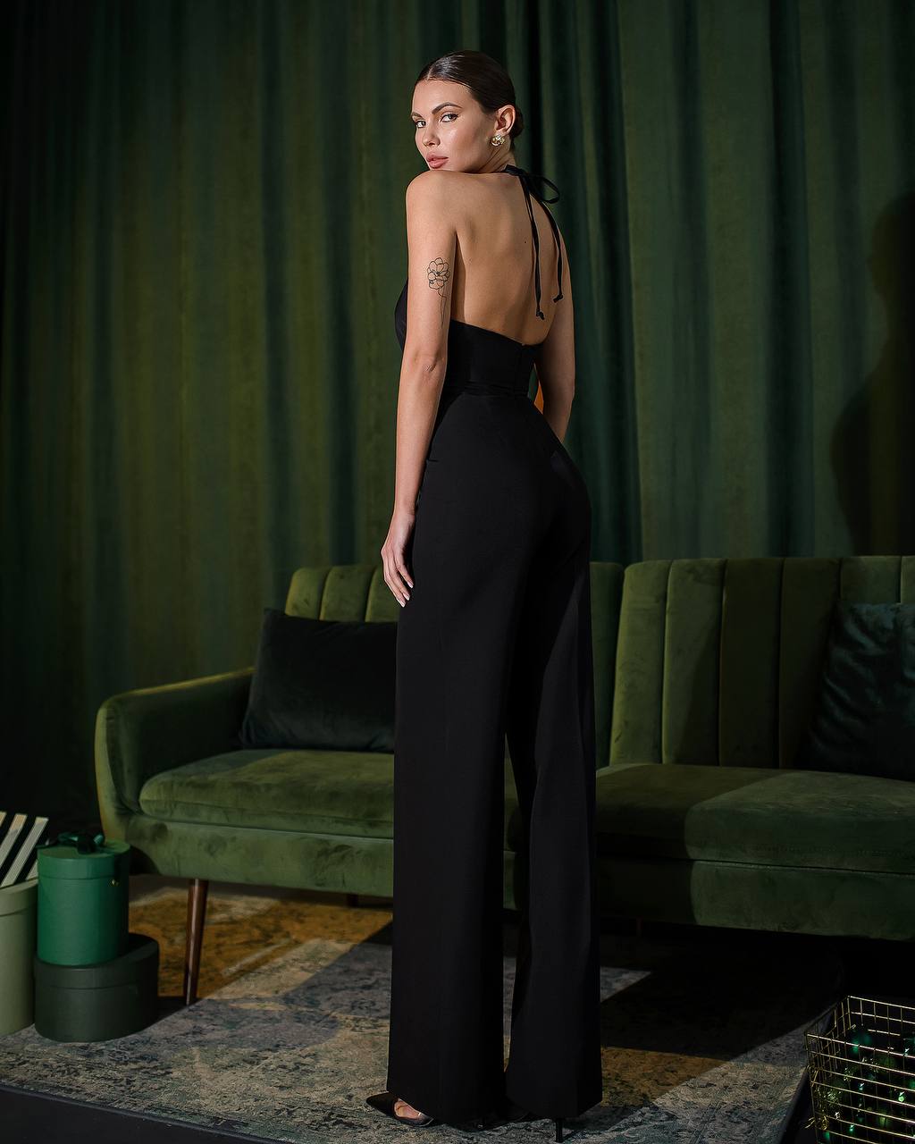 a woman in a black jumpsuit standing in front of a green couch